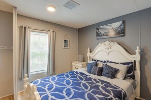 Quarto com cama grande, mesa de cabeceira, janela com cortinas e quadro na parede.