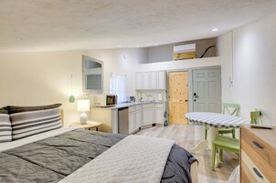 Una habitación compacta con cama, mesita de noche, lámpara y vista a una kitchenette.