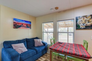 Una habitación con un sofá azul, una mesita roja con estampado de cuadros y dos sillas verdes.