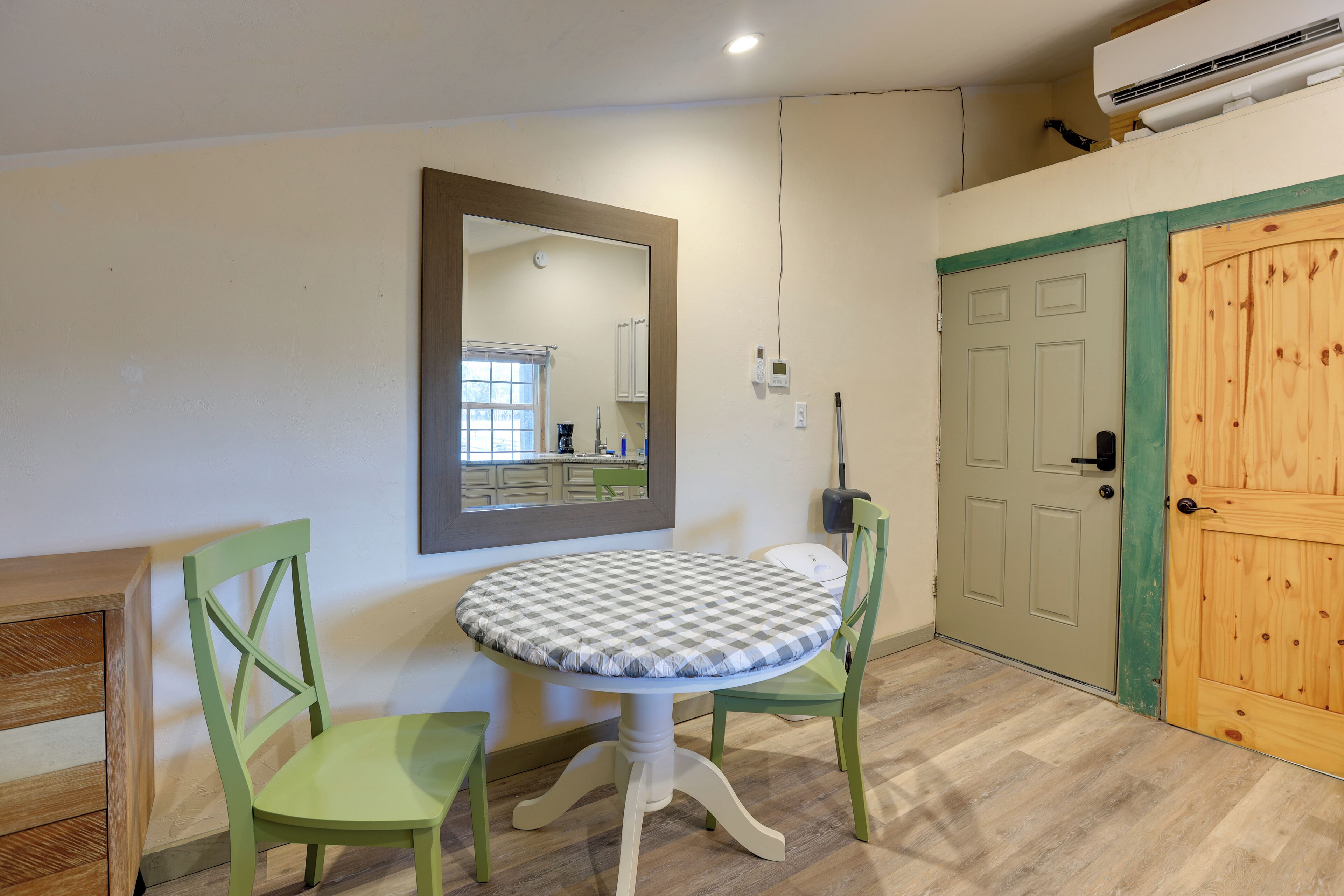 A room with a round table, two chairs, a mirror, a wooden door, and a small cabinet.
