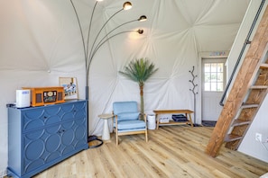A tented room with a blue cabinet, a blue chair, a small table, a plant, and a ladder.