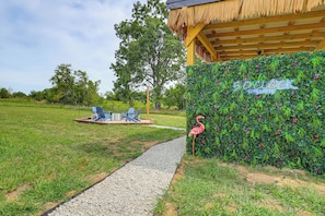 A pathway leading to a seating area with chairs and a table, a thatched-roof structure, and a wall with a sign reading '50 Cocks'.