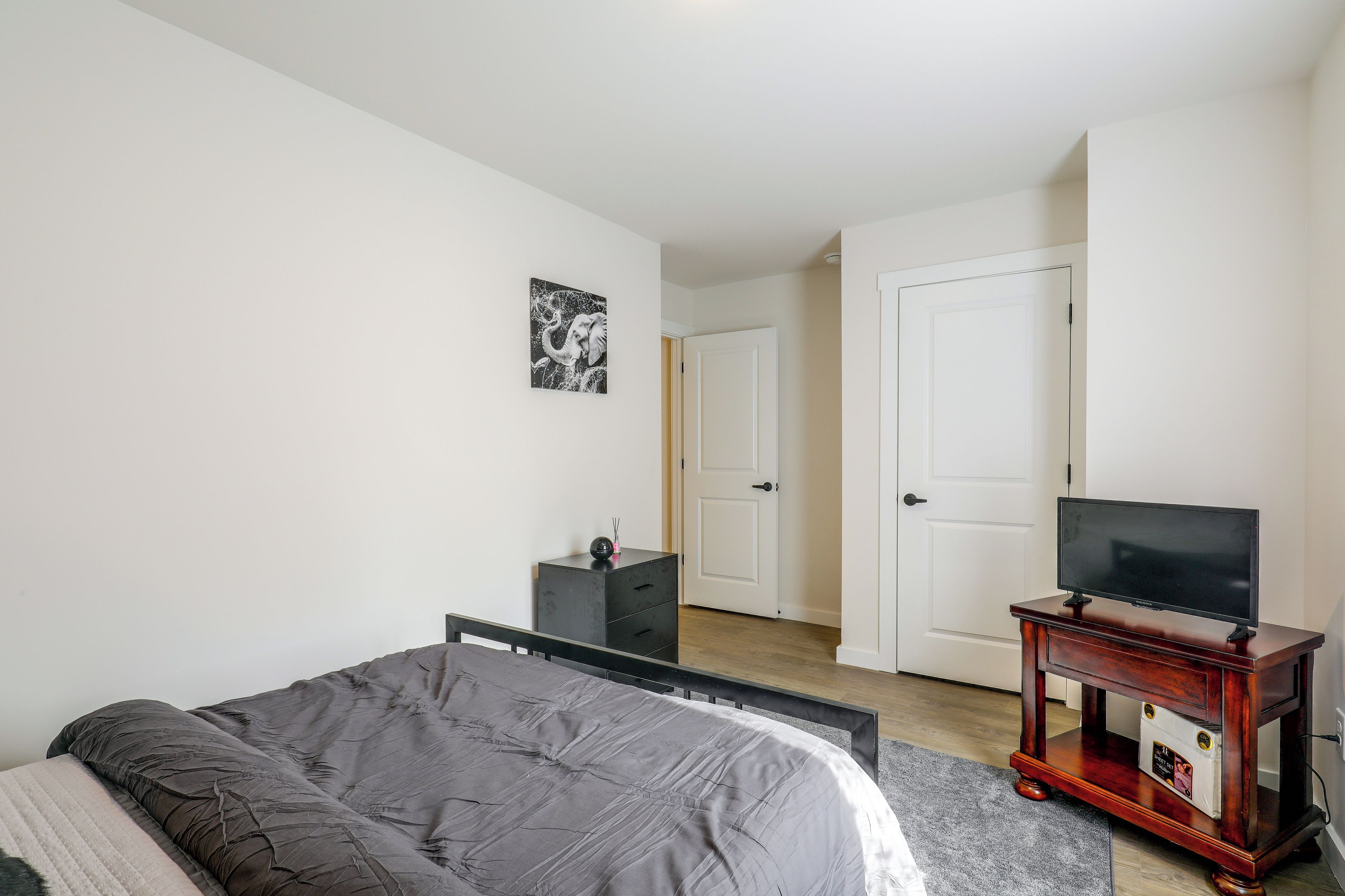 A bedroom with a bed, a television on a stand, a dresser, and a door leading to another room.