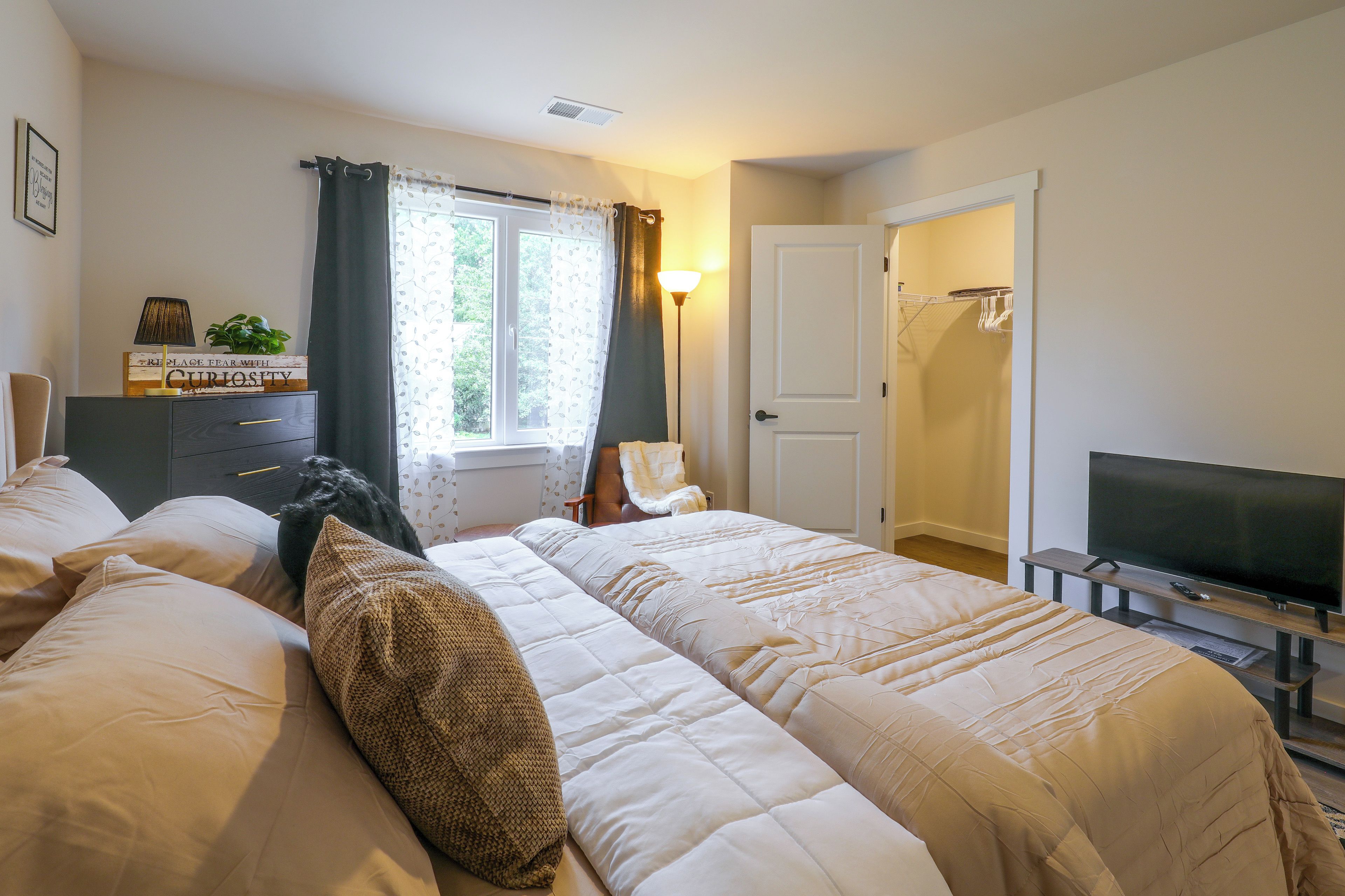A hotel room with two beds, a television, a desk with a lamp, and a window with curtains.