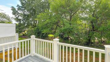 A wooden deck with white railings overlooking a grassy area with trees.