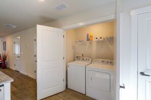 A laundry room with two stacked washer and dryer units, a shelf with cleaning supplies, and a door leading to another room. - Hickory Townhome w/ Balcony: 2 Mi to Downtown (Hickory)