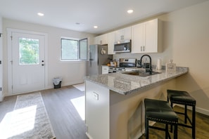 A modern kitchen with white cabinets, a granite countertop, stainless steel appliances, and a small bar area with stools. - Hickory Townhome w/ Balcony: 2 Mi to Downtown (Hickory)