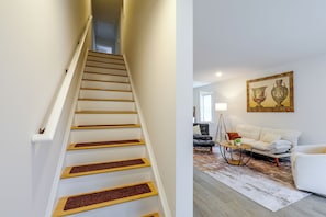 Un escalier avec des marches en bois et des murs blancs, menant à une pièce où se trouvent un canapé blanc, une table basse et un tableau accroché au mur.