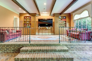 A spacious living area with a fireplace, a television, and a large window overlooking greenery.