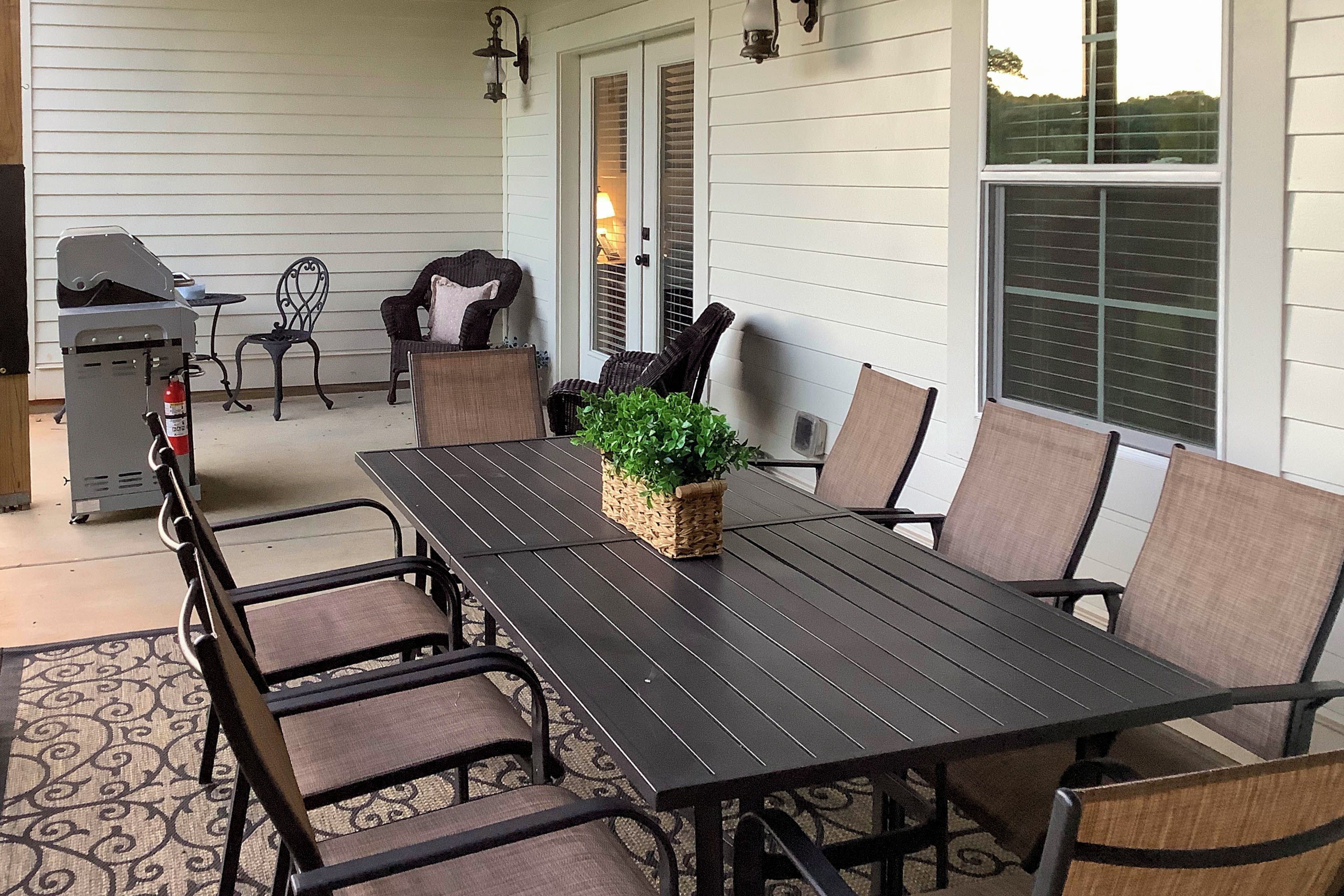 An outdoor patio with a dining table, chairs, a grill, and a potted plant.