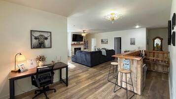 A modern living space with a wooden floor, a black sofa, a dining area with a bar, and a mounted TV.