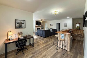 A modern living space with a wooden floor, a black sofa, a dining area with a bar, and a mounted TV.