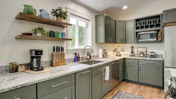 A modern kitchen with green cabinets, a marble countertop, and a window providing natural light.