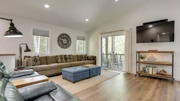 A modern living room with a sectional sofa, a leather couch, a flat-screen TV, and a large window with blinds.
