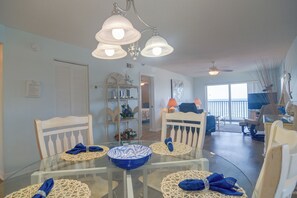 A dining area with a glass table, white chairs, and blue napkins. - Unit w/ Stunning Gulf Views! Steps to Pool & Beach (Madeira Beach)