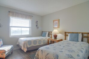 A room with two beds, a window with blinds, a bedside table with a lamp, and a wall decoration. - Unit w/ Stunning Gulf Views! Steps to Pool & Beach (Madeira Beach)