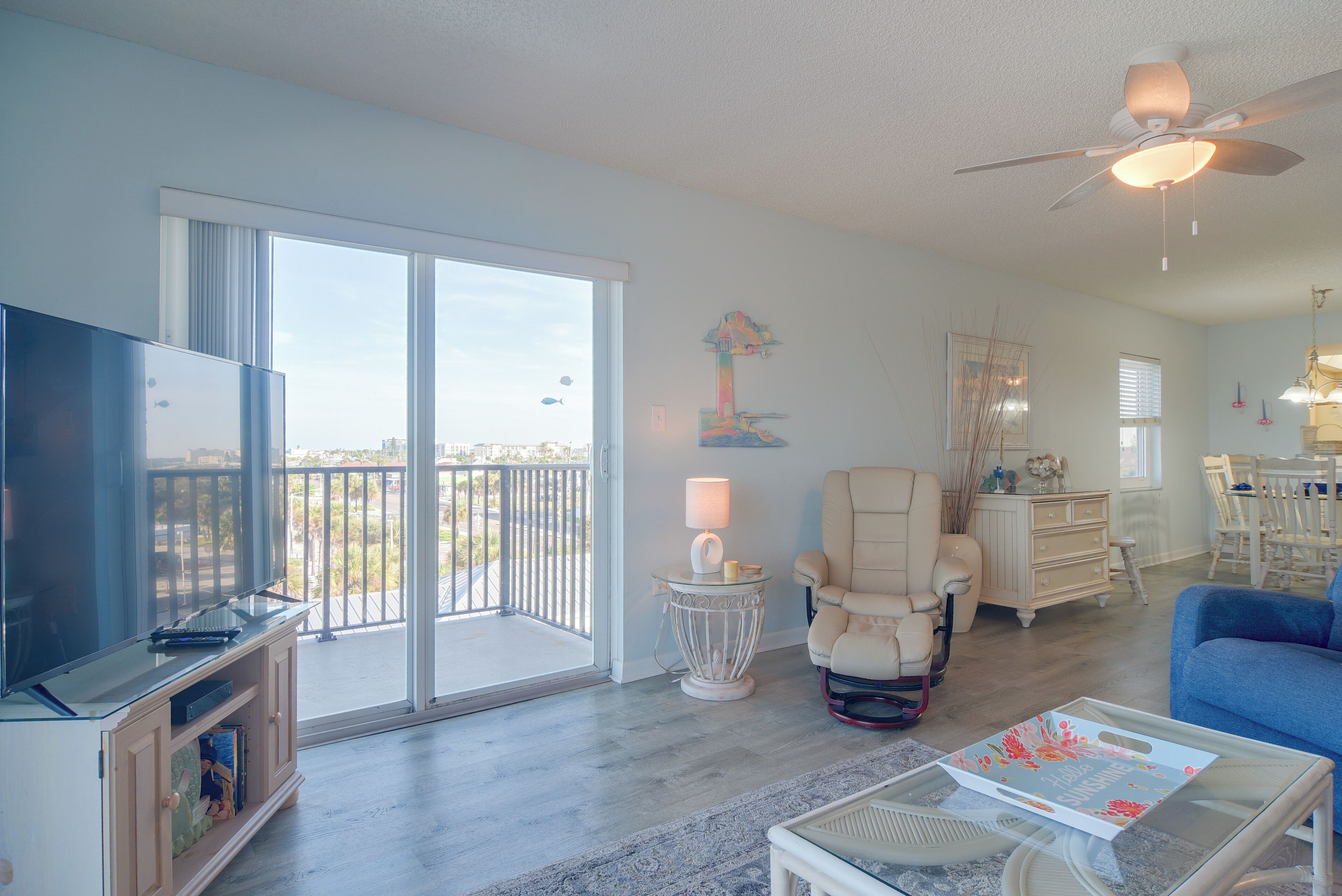 A spacious living room with a television, a chair, a coffee table, and a balcony with a view.