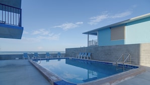 An outdoor swimming pool with a view of the sea, a covered seating area, and a building with a blue exterior. - Unit w/ Stunning Gulf Views! Steps to Pool & Beach (Madeira Beach)