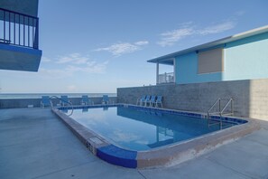 An outdoor swimming pool with a view of the sea, a covered seating area, and a building with a blue exterior. - Unit w/ Stunning Gulf Views! Steps to Pool & Beach (Madeira Beach)