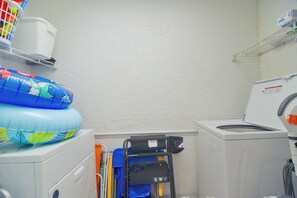 Et vaskerum med vaskemaskine, tørretumbler og en lille hylde med en kurv.