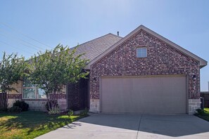 A two-story brick house with a garage, a small window on the second floor, and a tree in the front yard. - Family Home 7 Mi to University of North Texas! (Krum)