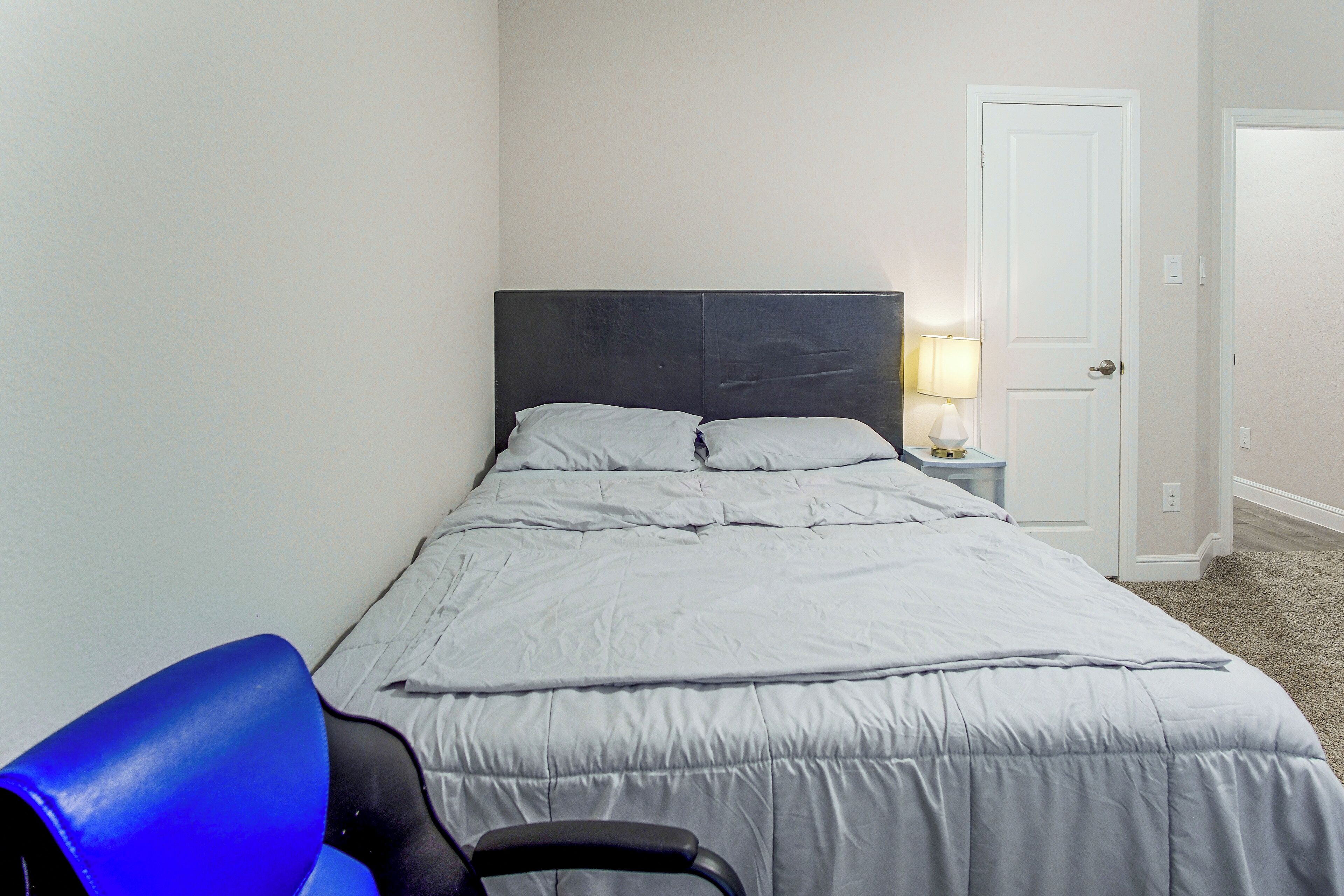A bedroom with a bed, a nightstand with a lamp, and a chair.