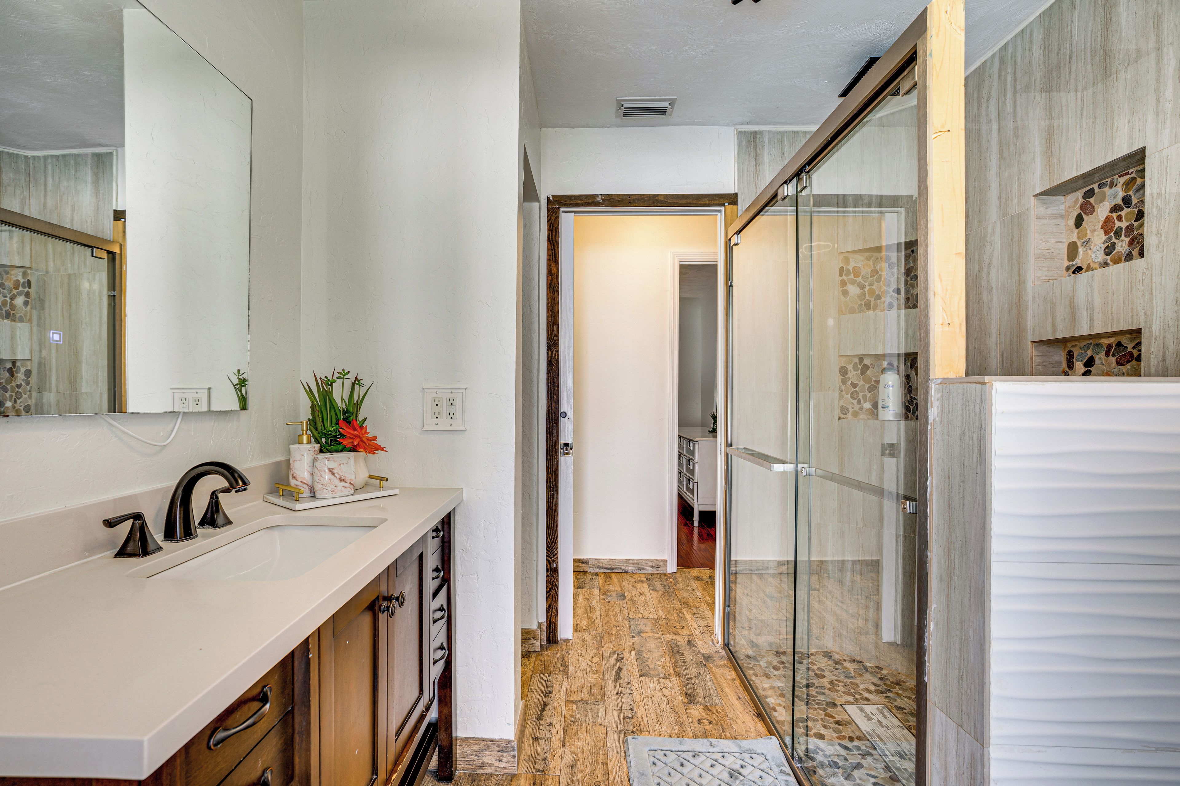 A modern bathroom with a large mirror, a sink with a faucet, a shower area with glass doors, and a wooden floor.