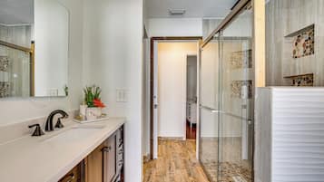 A modern bathroom with a large mirror, a sink with a faucet, a shower area with glass doors, and a wooden floor.
