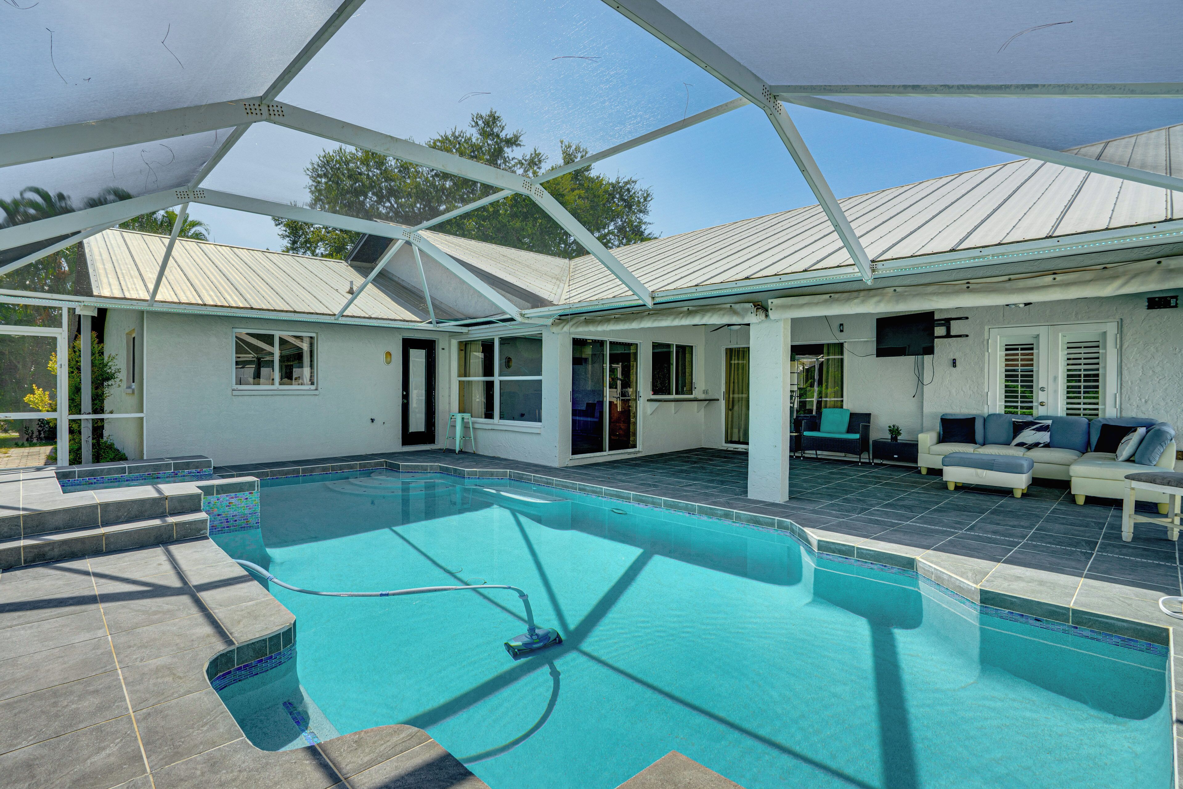 A covered outdoor swimming pool with a patio area, a covered seating area, and a television mounted on the wall.