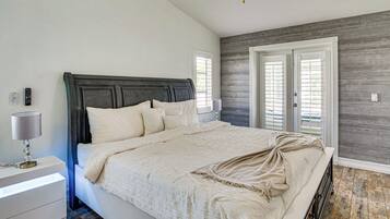 A bedroom with a large bed, bedside table, lamp, and a view of the outside through a door.
