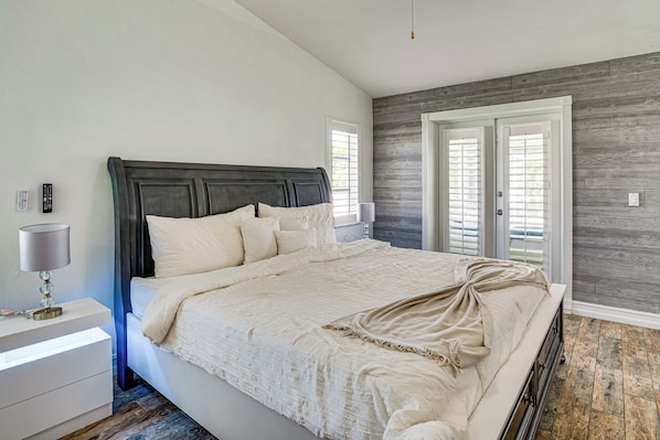 Un dormitorio con una cama grande, mesita de noche, lámpara y vista al exterior por una puerta.
