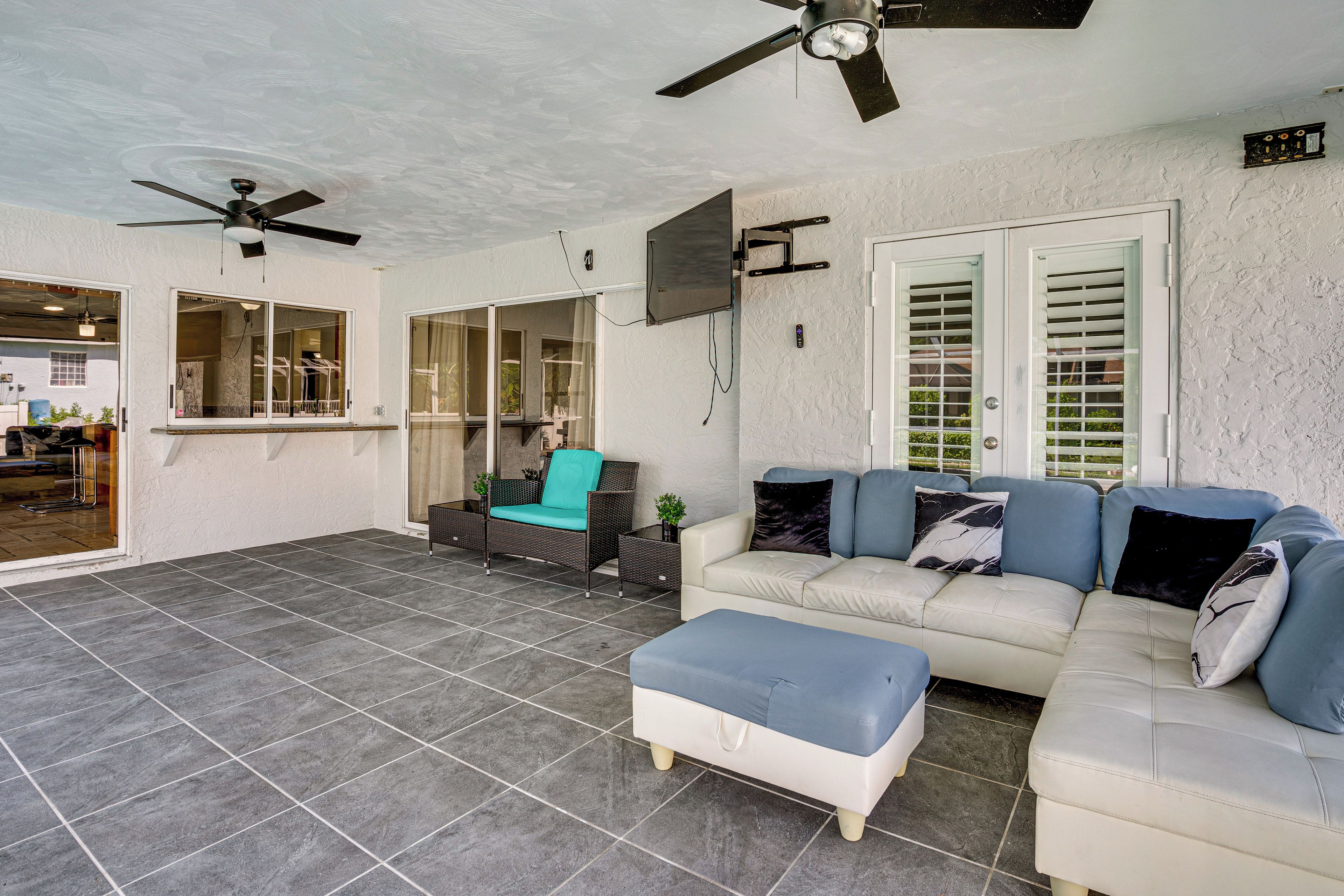 A covered patio area with a ceiling fan, a sofa set, a chair, and a TV mounted on the wall.