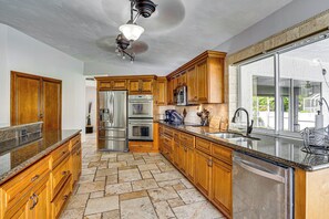 Una cocina con armarios de madera, electrodomésticos de acero inoxidable, encimera de granito y un amplio ventanal.