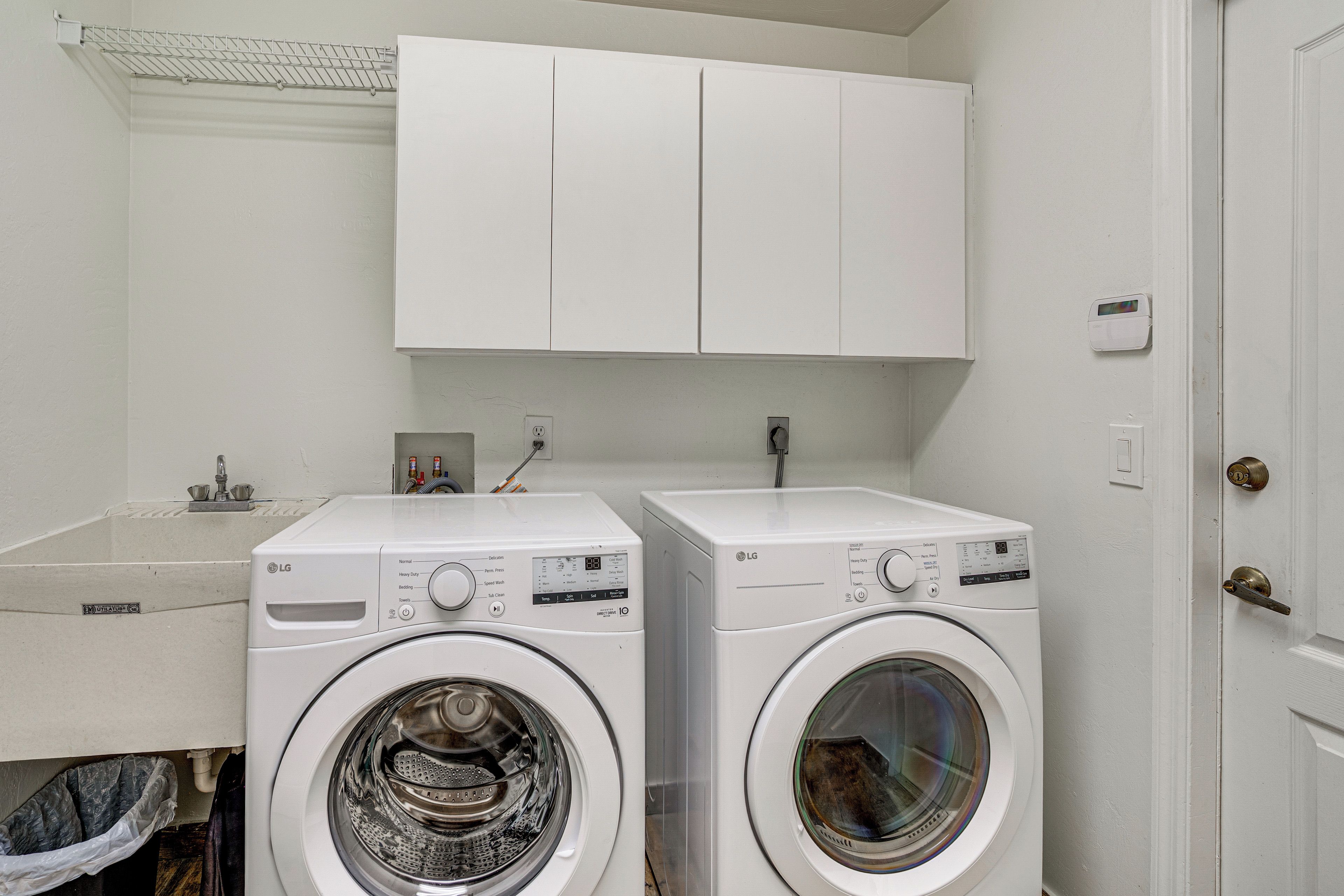 A laundry area with two white washing machines, a white sink, and a white door.