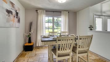A dining area with a table set for two, a vase with flowers, and a window with curtains.