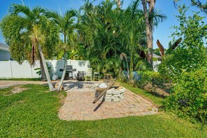 A paved patio area with a stone fire pit, surrounded by lush greenery and palm trees. - 2 Mi to Six Mile Preserve! Family Getaway w/ Pool (Fort Myers)
