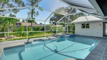 A swimming pool with a covered area, surrounded by a fence, and a view of neighboring houses.