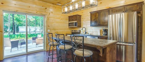 A modern kitchen with a stainless steel refrigerator, bar stools, and a large island.