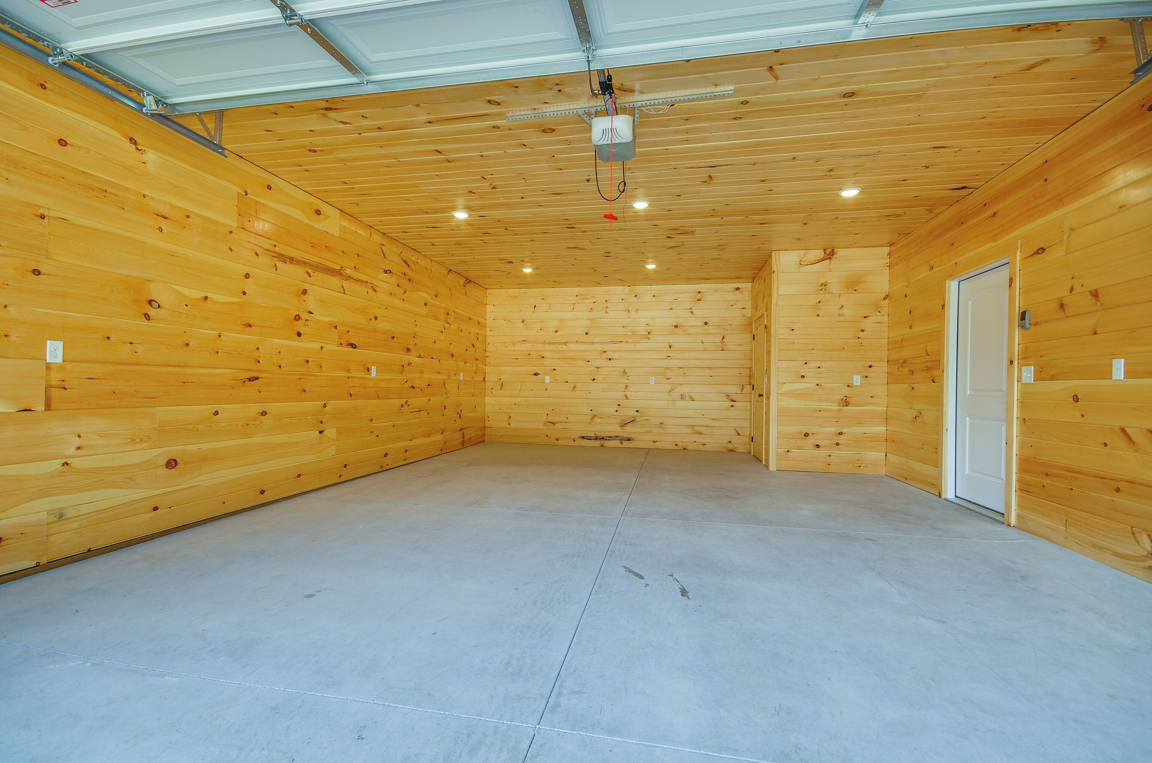A spacious room with wooden walls and a concrete floor, featuring a door and a ceiling-mounted light fixture.