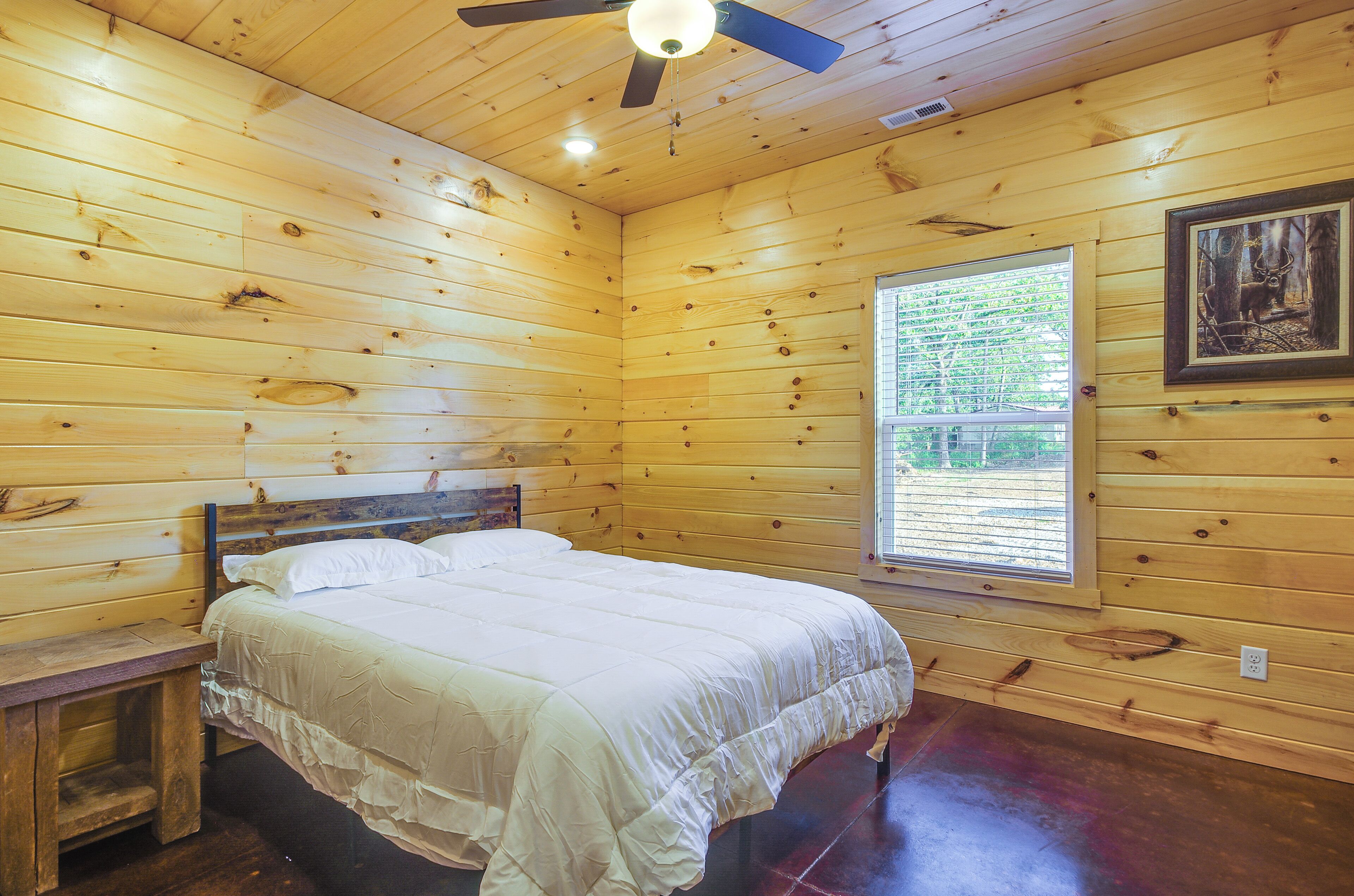 A wooden cabin room with a bed, a window, and a ceiling fan.