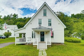 Une maison blanche à deux étages, dotée d’un porche à l’avant, d’un petit jardin et d’un drapeau américain.