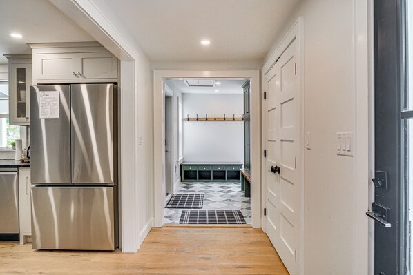 A modern kitchen with a stainless steel refrigerator, a wooden bench, and a hallway leading to a dining area.