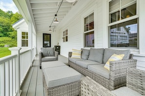A covered porch with a wicker sofa and ottoman, a railing, and a view of the surrounding greenery. - Modern Farmhouse Between Mount Snow & Stratton! (Wardsboro)