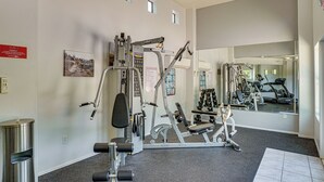 Ein Fitnessraum mit unterschiedlichen Trainingsgeräten, ein Spiegel, der die Geräte reflektiert, und ein Schild, das den Weg zu den Toiletten zeigt.