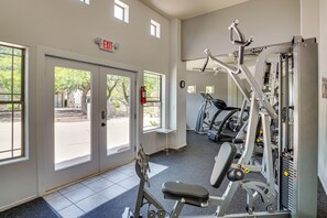 Ein Fitnessraum mit Trainingsgeräten, einer Tür mit der Aufschrift 'EXIT' und Fenstern mit Blick ins Freie.