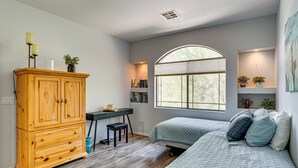 Ein Schlafzimmer mit Holzschrank, Schreibtisch, Stuhl, großem Fenster und einem Bett mit Kissen.