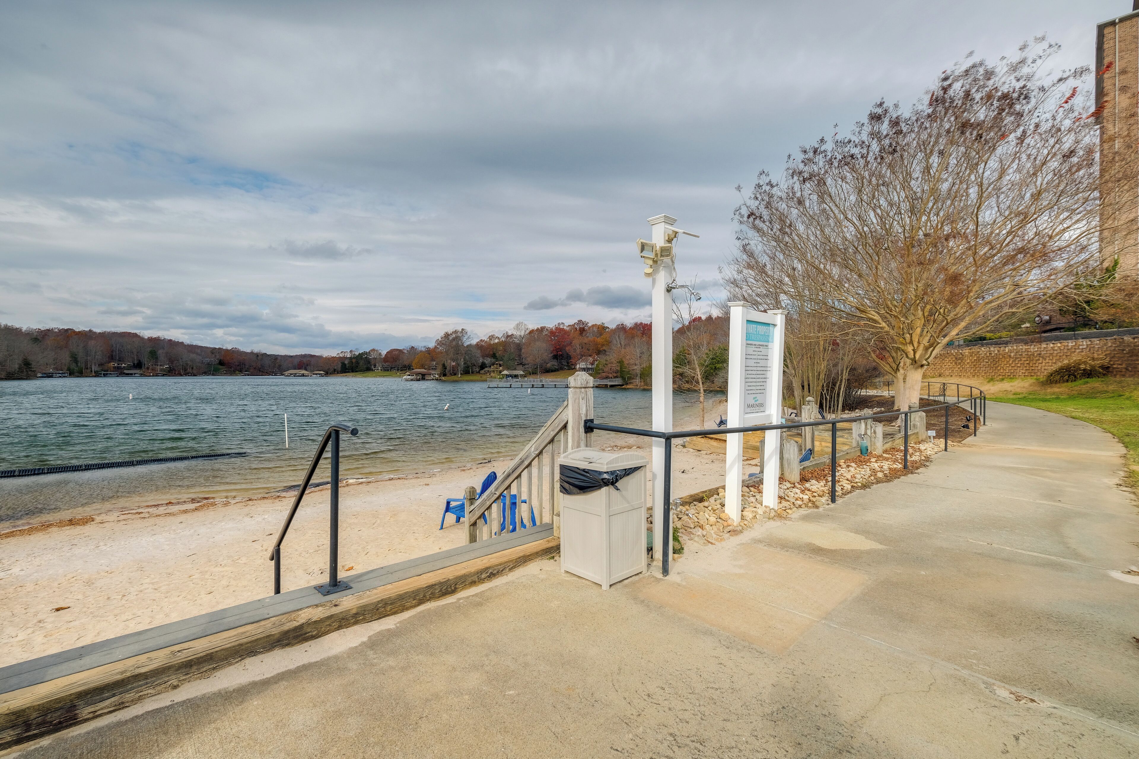 A waterfront walkway with a bench, trash can, and informational sign.