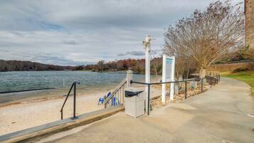 A waterfront walkway with a bench, trash can, and informational sign.