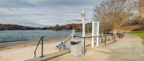 A waterfront walkway with a bench, trash can, and informational sign.