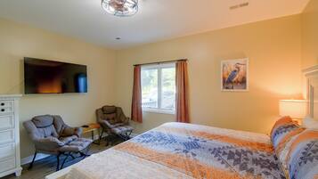 A bedroom with a bed, two chairs, a TV, a window with curtains, and a painting on the wall.